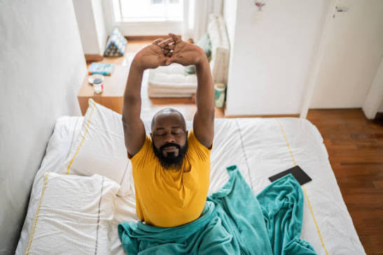 Well-rested young Nigerian man stretching beside a sunny window in the morning